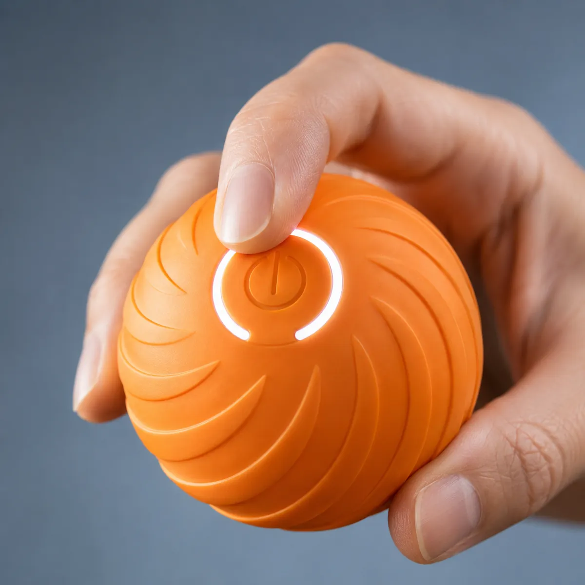 An index finger pressing the illuminated circular button on the orange self-rolling ball